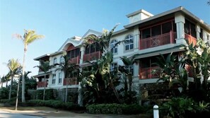 A multi-story building with balconies, surrounded by tropical vegetation.