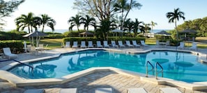 A swimming pool with lounge chairs and umbrellas, surrounded by palm trees and a view of the ocean. - Sanibel Island | Relaxing Coastal Retreat | Pool + Beach | 2BR (Sanibel Island)
