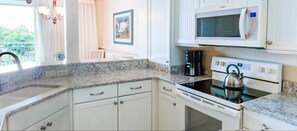 A kitchen with white cabinets, a microwave, an oven, and a kettle. - Sanibel Island | Relaxing Coastal Retreat | Pool + Beach | 2BR (Sanibel Island)