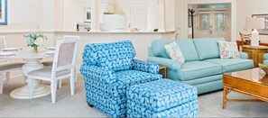 Una sala de estar con un sillón azul estampado, un sofá color turquesa y una mesa de centro de madera.