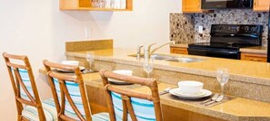 Una cocina con encimera de granito, estufa negra y salpicadero de azulejos.