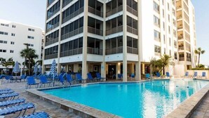 Ein Hotelpoolbereich mit mehreren Balkonebenen, blauen Liegestühlen und einem klaren, blauen Pool.