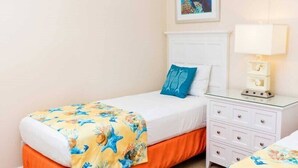 Une chambre d’hôtel avec deux lits simples, une table de chevet avec une lampe et une petite commode.