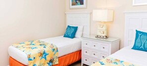 Una habitación de hotel con dos camas individuales, una mesita de noche con lámpara y un pequeño aparador.