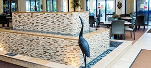 A reception area with a stone wall, a black bird sculpture, and a seating area with tables and chairs.