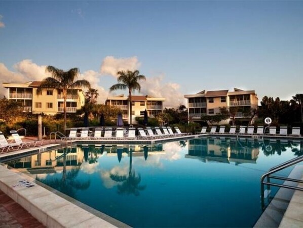 A swimming pool with lounge chairs, a clear sky, and a building with balconies in the background.