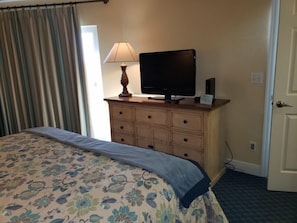 A hotel room with a bed, a television on a dresser, and a door. - Sanibel Island | Family Beach Retreat | Pool + Beach | 2BR (Sanibel Island)
