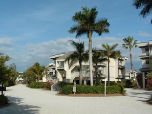 A residential area with multi-story buildings, palm trees, and a gravel driveway. - Sanibel Island | Family Beach Retreat | Pool + Beach | 2BR (Sanibel Island)