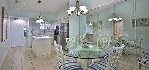 Une cuisine moderne dotée d’un îlot central, de meubles blancs, d’appareils électroménagers en acier inoxydable et d’un coin repas avec une table en verre et des chaises à rayures.