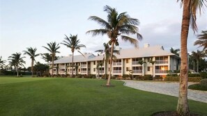Un hôtel à plusieurs étages, doté d’un toit plat, entouré d’une pelouse bien entretenue et de palmiers.