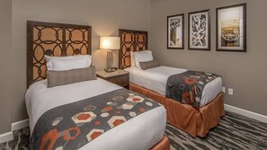 Habitación de hotel con dos camas, cada una con una colcha estampada y cabeceros a juego. Un mesita de noche con lámpara se encuentra entre las camas, y hay dos obras de arte enmarcadas en la pared.