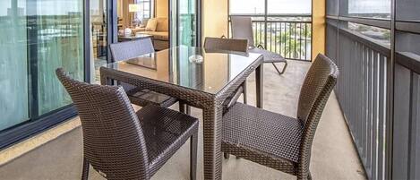 Een balkon met rieten meubilair, een glazen tafel en uitzicht op het interieur.