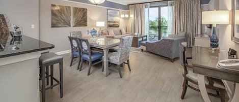 Una habitación de hotel moderna con zona de comedor, sofá y balcón con cortinas.