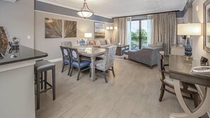 Una habitación de hotel moderna con zona de comedor, sofá y balcón con cortinas.