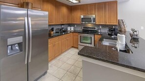 A modern kitchen with stainless steel appliances, wooden cabinets, and a granite countertop. - Marco Island | Family Waterfront Stay | Pool + Marina | 3BR Sleeps 8 (Marco Island)