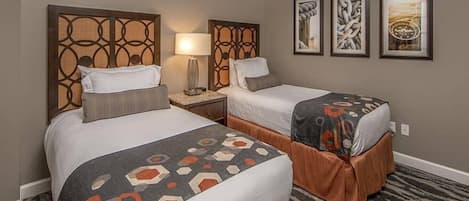Una habitación de hotel con dos camas, una mesita de noche, una lámpara y cuadros en la pared.