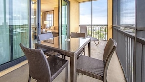 En balkon med fletmøbler, et glasbord og udsigt over bybilledet.