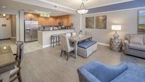 A modern kitchen with a central island, dining area with chairs, and a living room with a sofa and a lamp.