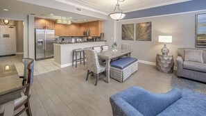 Una cocina moderna con una isla central, comedor con sillas y sala de estar con sofá y lámpara.