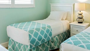 A room with two beds, each with a patterned bedspread, a bedside table with a lamp, and a window with blinds.