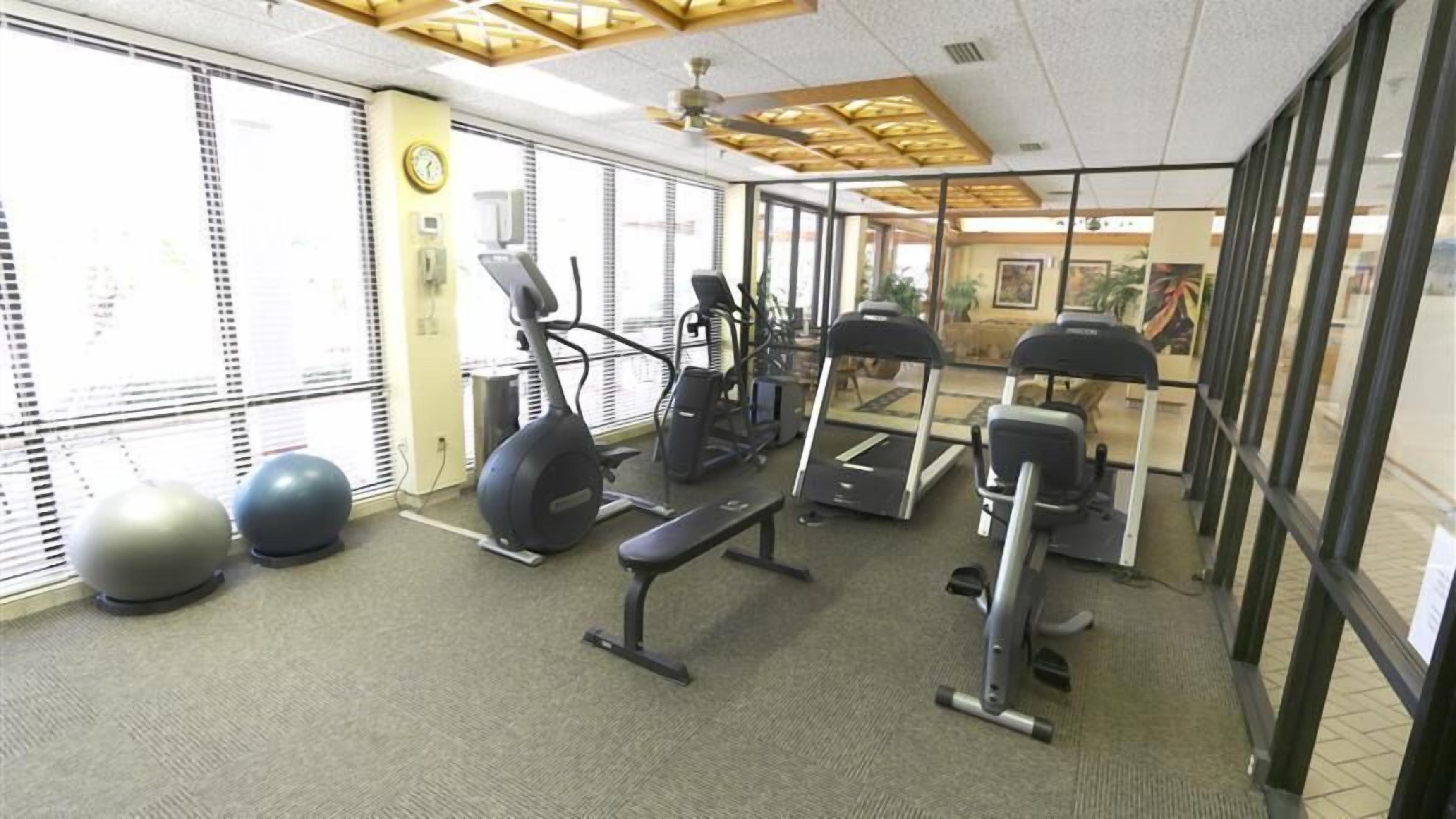 Un gimnasio con equipo de ejercicio, ventanas amplias y un reloj en la pared.