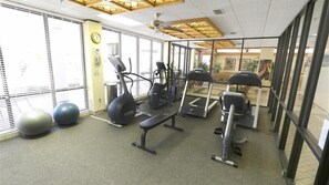 A gym with exercise equipment, large windows, and a clock on the wall.