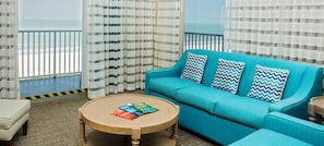 Una habitación con sofá azul, cortinas a rayas, una mesa de centro redonda de madera y vista a la playa.