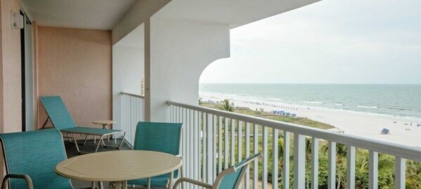 A balcony with a view of the beach, a round table, and two chairs.