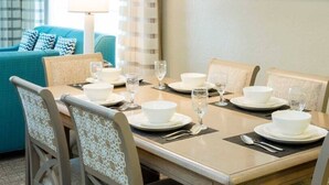 A dining table set with white plates, bowls, and glasses, surrounded by chairs with patterned upholstery.