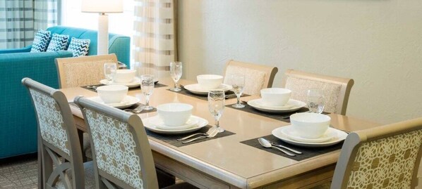 Comedor con una mesa dispuesta para cuatro personas, incluyendo platos, fuentes y vasos blancos.