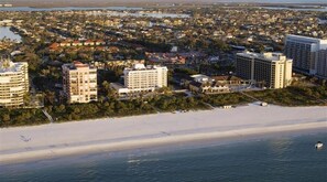 An aerial view of a coastal city with a beachfront, including several multi-story buildings and a sandy beach.