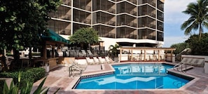 Zona de piscina de un hotel con una pileta grande, sillas de descanso y un edificio de diseño moderno.