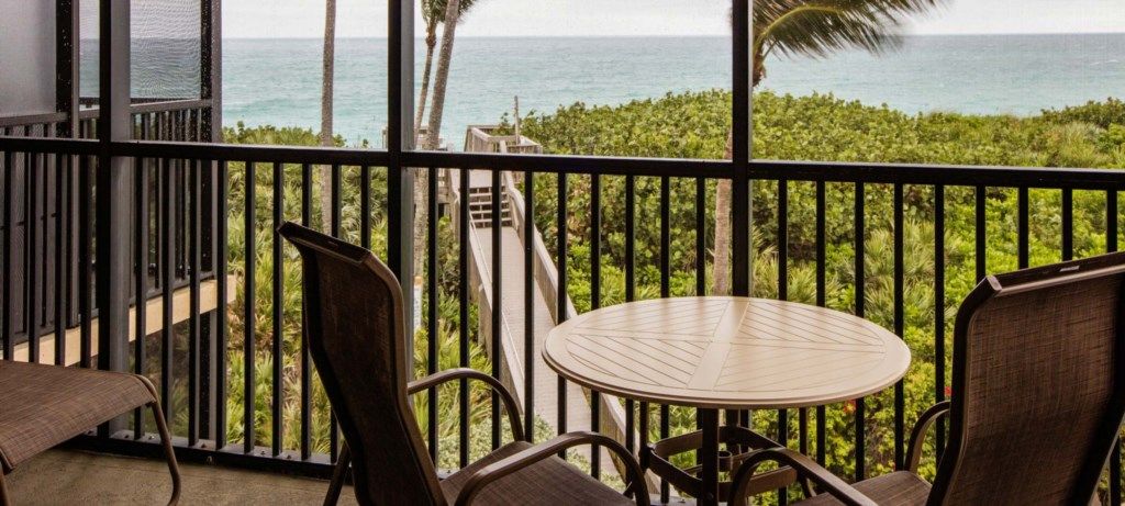Un balcon avec une table ronde et des chaises, offrant une vue sur un paysage verdoyant et luxuriant et sur l’océan.