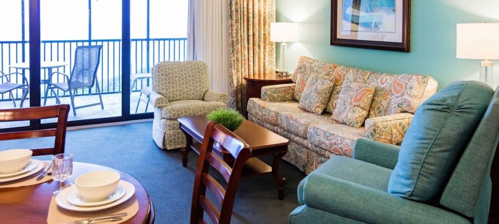 Une chambre d’hôtel équipée d’un canapé, d’un fauteuil, d’une table à manger et offrant une vue sur l’extérieur.