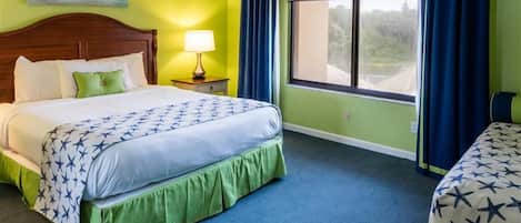 A hotel room with a large bed, a nightstand, a window with curtains, and a view of the outdoors.