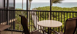 Ein Balkon mit rundem Tisch und Stühlen, der auf eine üppige grüne Landschaft und den Ozean blickt.
