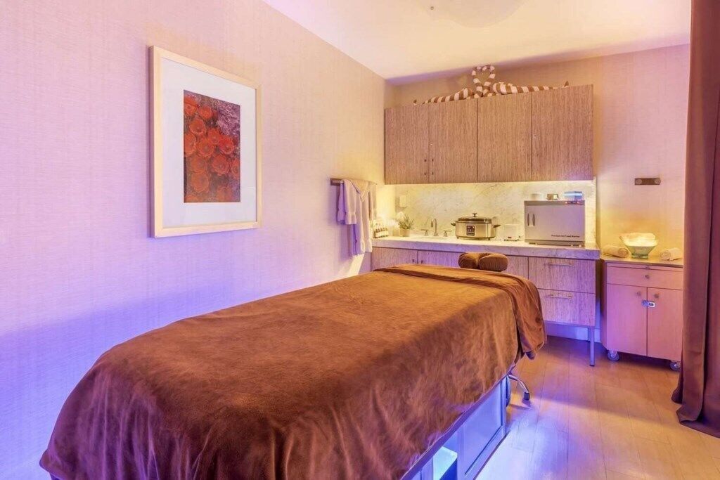 Een slaapkamer met een enkel bed, een klein kitchenette en een lijst met een kunstwerk aan de muur.