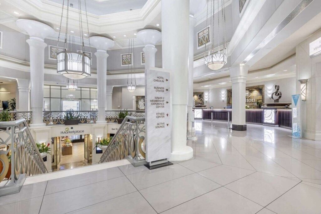 Un amplio vestíbulo de hotel con una escalera central, un gimnasio y un centro de negocios.