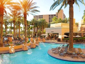 A pool area with lounge chairs and palm trees, surrounded by a building with a sign that reads "WAVES". - Las Vegas | Pool & Strip Access | 2BR Plus (Las Vegas)