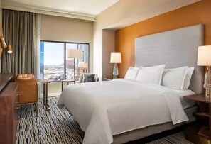 A hotel room with a large bed, a desk, a chair, and a view of a cityscape through a large window. - Las Vegas | Pool & Strip Access | 2BR Plus (Las Vegas)