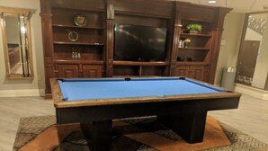 Una mesa de billar en una habitación con armarios de madera y un televisor.