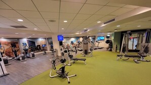 Un gimnasio con varios equipos de ejercicio, incluyendo cintas de correr, bicicletas estáticas y máquinas de pesas.