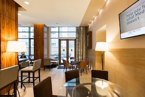 Vestíbulo de hotel con una mesa de vidrio, sillas, mostrador de recepción y una pantalla grande que muestra información sobre Medicare.