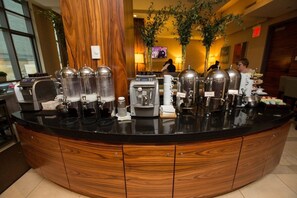A coffee station with multiple espresso machines and dispensers, a wooden counter, and a TV in the background. - New York City | Elegant Manhattan Stay | Central Location | Studio Premier (New York)