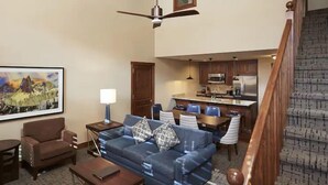 A living room with a sofa, a coffee table, and a TV. There is a staircase leading to an upper level. - Park City | Crew Snow Hub | Pool + Hot Tub | 3BR Sleeps 8 (Park City)