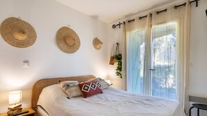 Un dormitorio con cama, mesita de noche, lámpara y ventana con cortinas.
