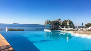 Una piscina infinita de color azul intenso con tumbonas blancas y vistas al mar.