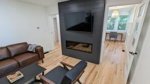 A modern living room with a flat-screen TV mounted on a dark wall, a fireplace, a brown leather sofa, and a wooden coffee table.
