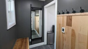 A modern bathroom with a wooden bench, a mirror, a towel rack, and a small trash bin.