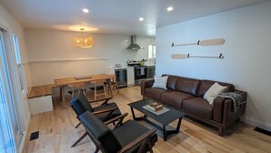 A modern living room with a brown leather sofa, black chairs, a wooden coffee table, and a dining area with a wooden table and chairs.